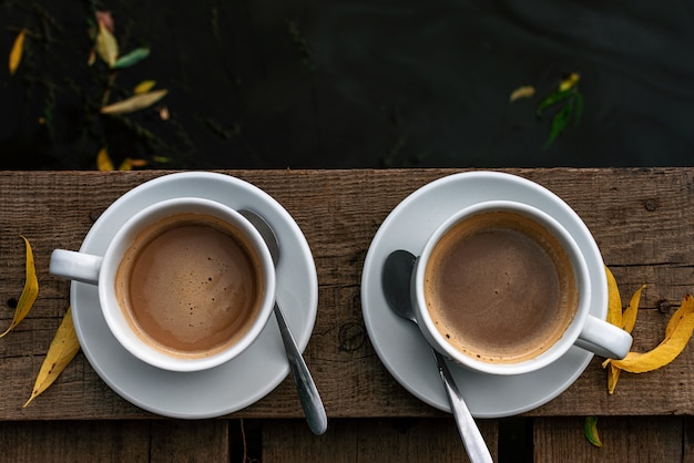 Foto zwei weiße tassen kaffee mit milch auf einem holzboden über dem fluss