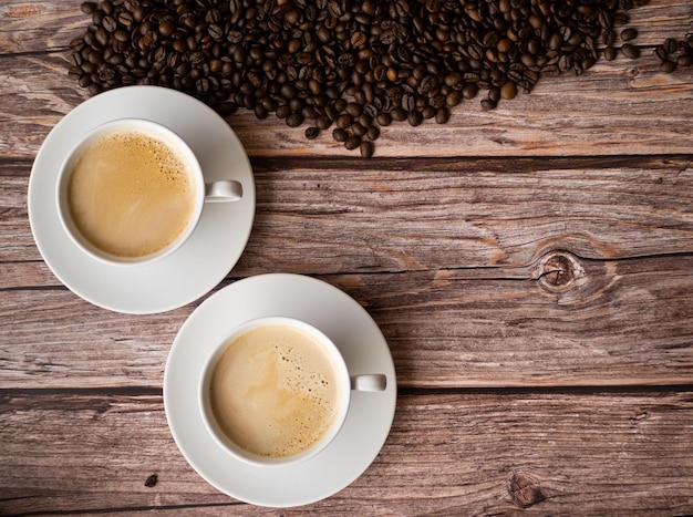 Zwei weiße Tassen Kaffee mit Milch auf Holztisch mit Platz zum Schreiben