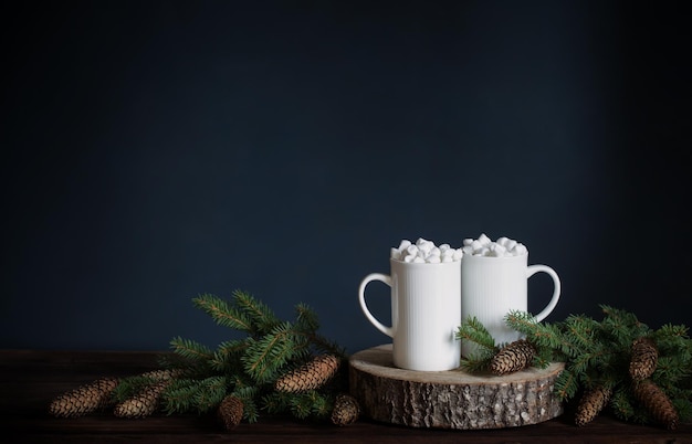 Zwei weiße Tassen mit Getränken mit Marshmallows und Weihnachtsdekorationen auf dunklem Hintergrund