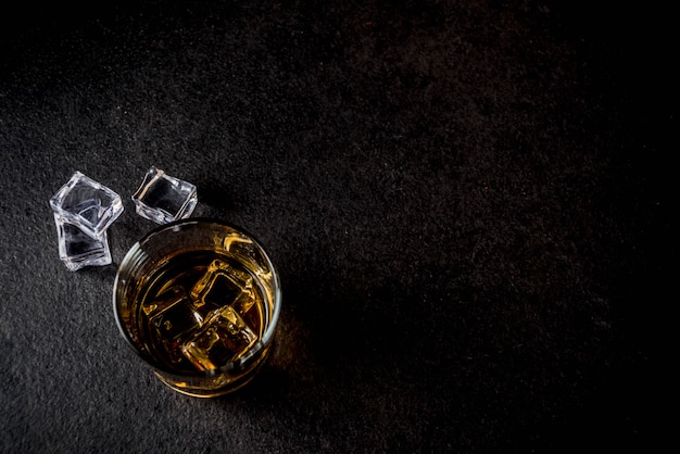 Zwei Whisky-Schnapsgläser auf dunklem Holztisch, mit Eiswürfeln,