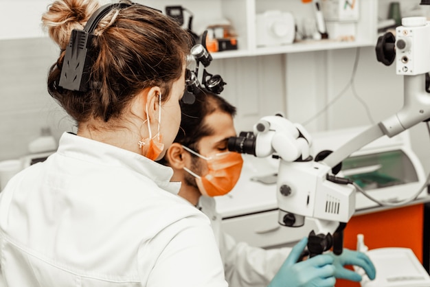 Zwei Zahnärzte behandeln einen Patienten. Berufsuniform und Ausrüstung eines Zahnarztes. Gesundheitswesen Ausstattung des Arbeitsplatzes eines Arztes. Zahnheilkunde