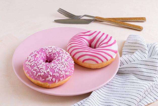 Zwei zuckerüberzogene rosa Donuts auf einem rosa Keramikteller