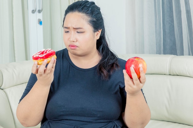 Zweifelhafte fette Frau, die Apfel und Donuts hält