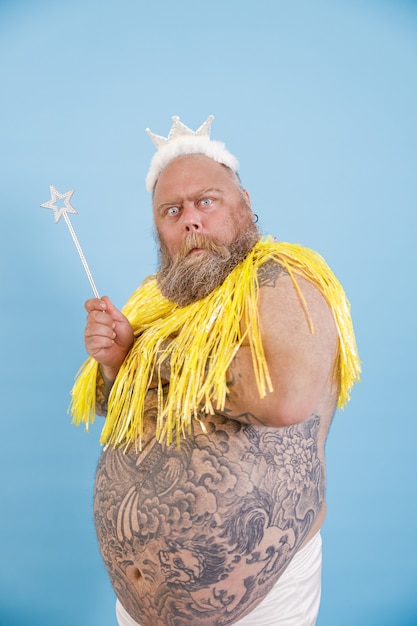 Foto zweifelnder mann in übergröße mit krone und zauberstab posiert auf hellblauem hintergrund