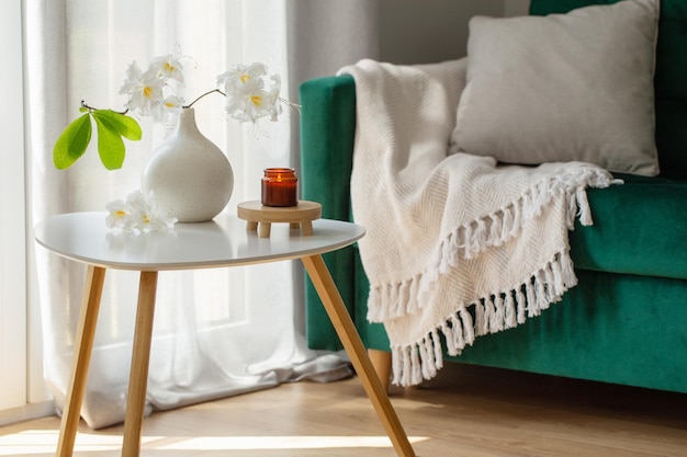 Zweig eines weißen Rhododendrons in einer Vase und brennende Kerzen in einem modernen, gemütlichen Interieur