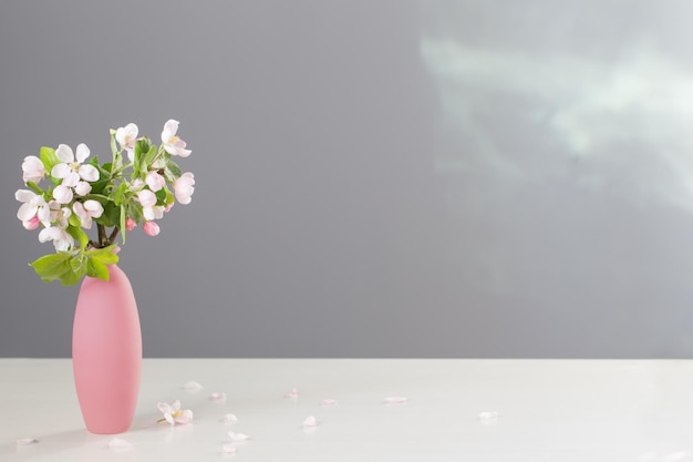 Zweige des Apfelbaums mit Blumen in rosa Vase auf weißem Tisch