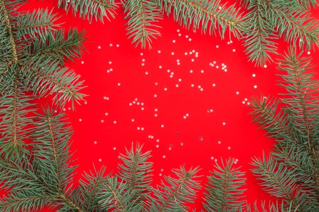 Zweige eines Weihnachtsbaumes auf Rot mit silbernen Konfetti-Sternen. Flach liegen.