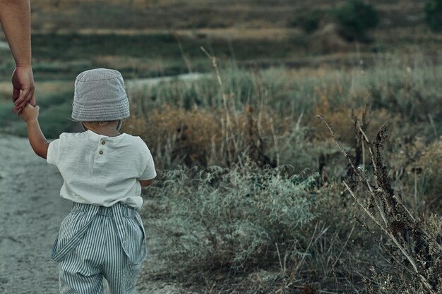 Zweijähriges Kind mit Hut geht eine Landstraße entlang
