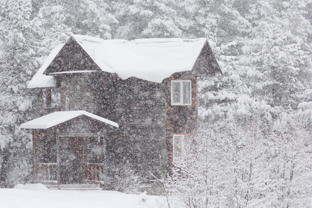 Zweistöckiges Holzhaus mit schneebedecktem Dach, das von Schneeflocken auf Schneeverwehungen verschwommen ist