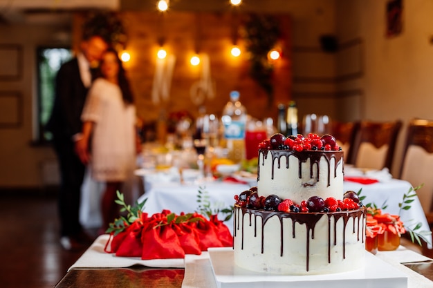 Zweistufige weiße Hochzeitstorte, dekoriert mit frischen roten Früchten und Beeren, in Schokolade getränkt