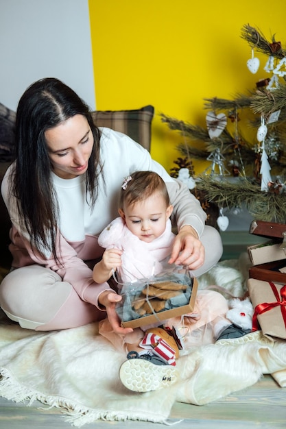 Zweiter Weihnachtstag und Auspacken von Weihnachtsgeschenkboxen süßes kleines Baby, Kleinkind, Mädchen und Mutter packen Geschenk aus