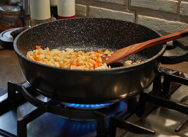 Zwiebeln und Karotten werden in der Pfanne auf dem Gasherd gebraten