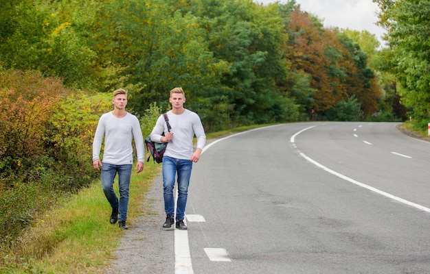 Zwillinge gehen die Straße entlang. Brüder Freunde Natur Hintergrund. Langer Weg. Abenteuer-Konzept. Jungs, die per Anhalter unterwegs sind. Autostopp für Touristenreisende. Transportprobleme. Männer Rucksack zu Fuß Straße.