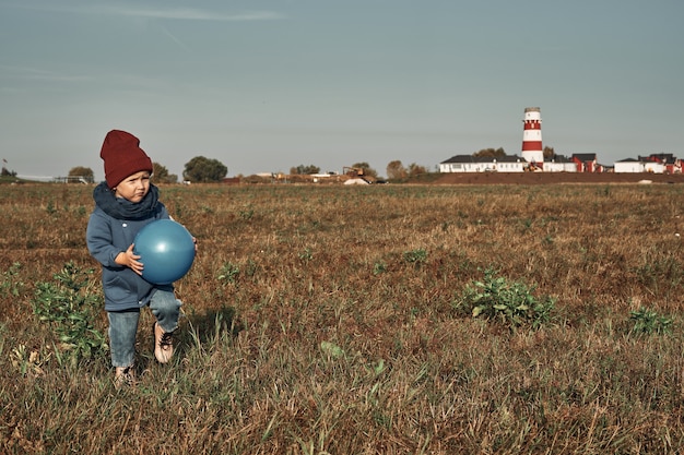 Zwillinge spielen Ball auf dem Feld, ein Leuchtturm im Hintergrund, Kinder zwei Jahre alt. Herbstspaziergänge in der Natur.