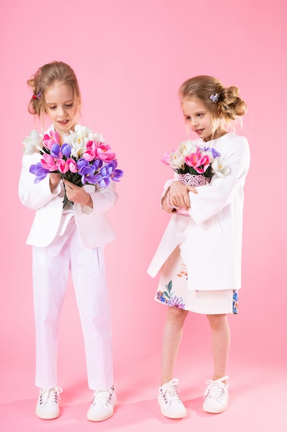 Zwillingsmädchen in leichter Kleidung mit Blumensträußen stehen auf Rosa.