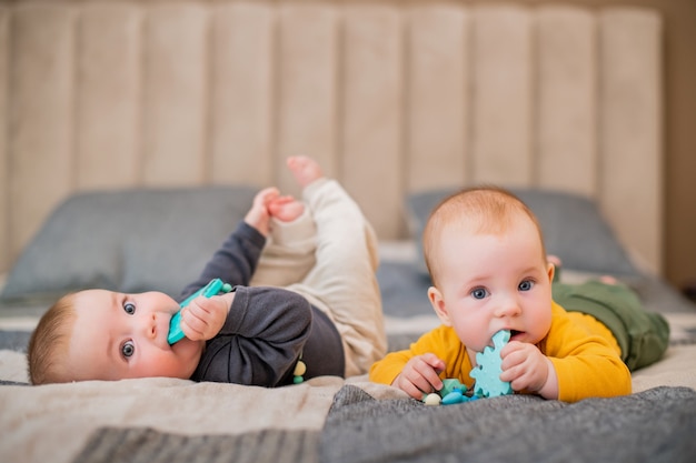 Zwillingsmädchenbabys liegen auf dem Bett und nagen an Beißringen