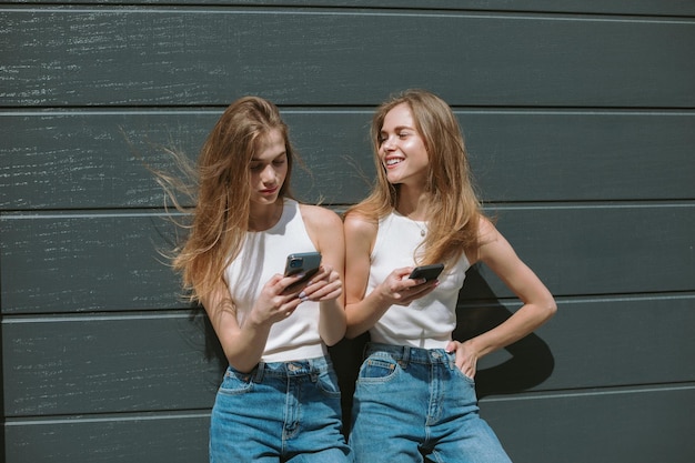 Zwillingsschwestern lachen über etwas, das sie auf Mobiltelefonen sehen.