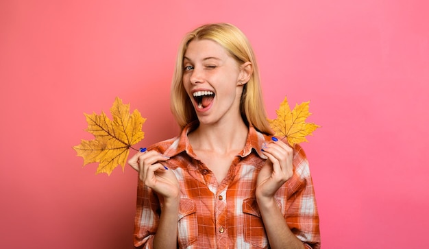 Zwinkerndes Mädchen mit gelben Ahornblättern Herbstmode glückliche Frau in Freizeitkleidung
