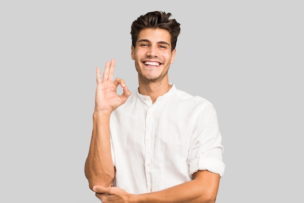 Zwinkert mit den Augen und hält eine Okay-Geste mit der Hand
