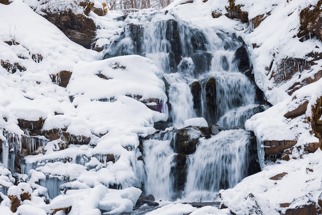 Zwischen den schneebedeckten Steinen fließt ein kleiner Wasserfall aus kaltem Wasser