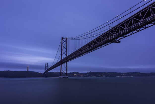 25 de Abril Bridge over the Tagus river surrounded by hills and lights in the evening