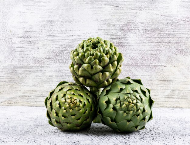 3 artichokes on a light gray . side view.