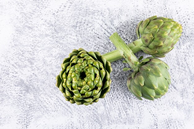 3 artichokes on light gray , side view.