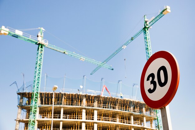 Знак ограничения в скорости 30 перед строительной площадкой против голубого неба