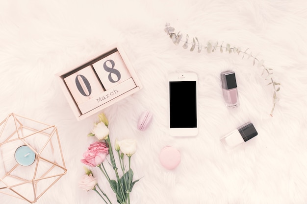 8 March inscription with smartphone, flowers and sweets on blanket 