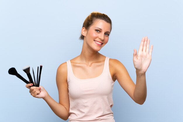 幸せな表情で手で敬礼化粧ブラシの多くを保持している若いブロンドの女性 プレミアム写真