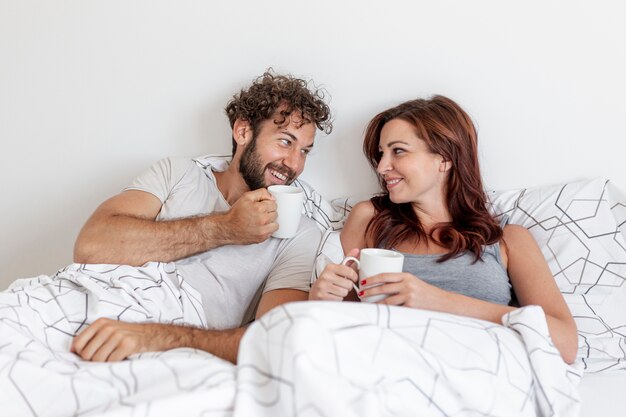 かわいいカップルがベッドの中でコーヒーを飲む 無料の写真
