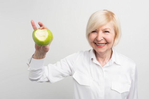 Красивая зрелая женщина, держащая укушенное зеленое яблоко в правой руке. она хочет показать, что у нее хорошие и крепкие зубы.