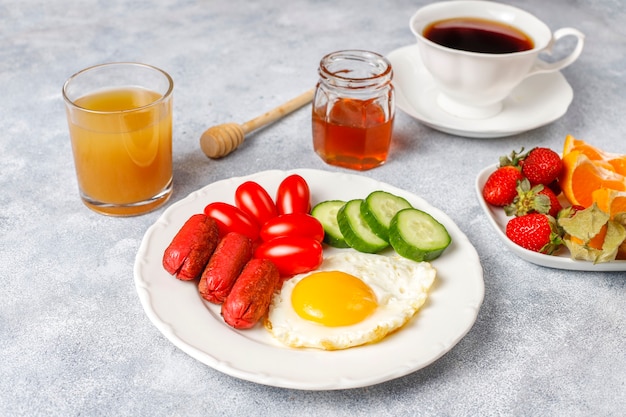 칵테일 소시지, 계란 후라이, 체리 토마토, 과자, 과일, 복숭아 주스 한 잔이 포함 된 조식 플레이트입니다.