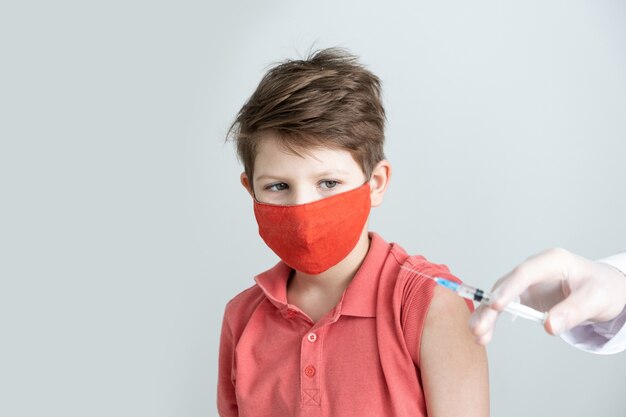 医療用マスクを着用した子供が、パンデミックでコロナウイルスの予防接種を受けています Premium写真