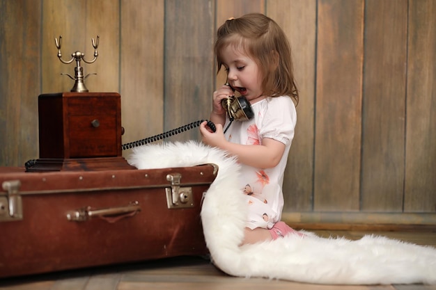 На полу сидит ребенок в ретро-интерьере и старый телефон. маленький ребенок путешественник в старинных украшениях. ребенок-путешественник звонит по телефону.
