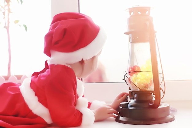 새해에 아이가 창 밖을 내다본다. 아이들은 산타 클로스를 기다리고 있습니다. 산타 옷을 입은 아이가 창가에 앉습니다.
