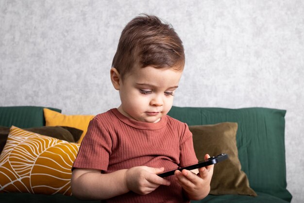 Ребенок играет по мобильному телефону на кровати у себя дома, портрет маленького мальчика