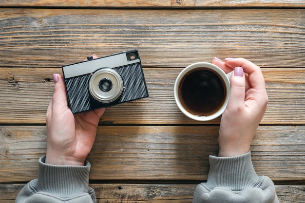 Бесплатное фото Чашка кофе и ретро-камера в женских руках на деревянном фоне