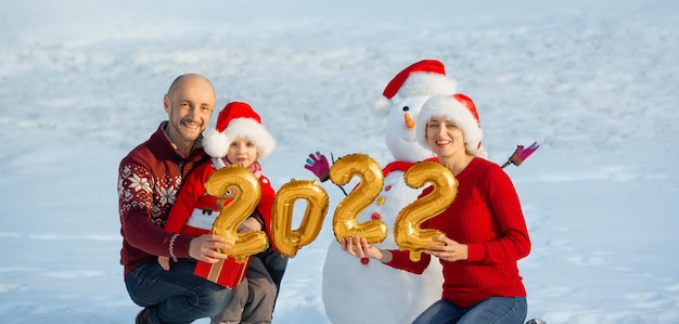 Семья держит фигурки предстоящего нового года рядом со снеговиком на рождество