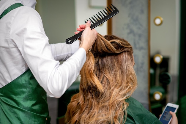Парикмахер расчесывает длинные каштановые волосы молодой женщины в салоне. Premium Фотографии