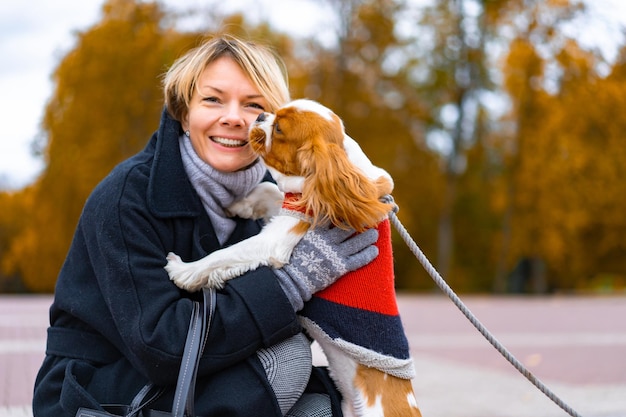 무료 사진 한 여성이 cavalier king charles spaniel과 함께 공원을 걷고 있습니다. 강아지와 함께 가을 공원에서 산책 하는 여자. 카발리에 킹 찰스 스파니엘