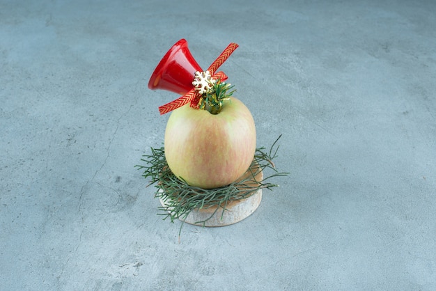 Свежее яблоко с красным рождественским колокольчиком на мраморе.