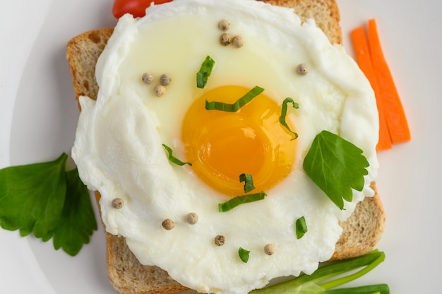 Бесплатное фото Жареное яйцо откладывают на тост, увенчанный семенами перца с морковью и зеленым луком.