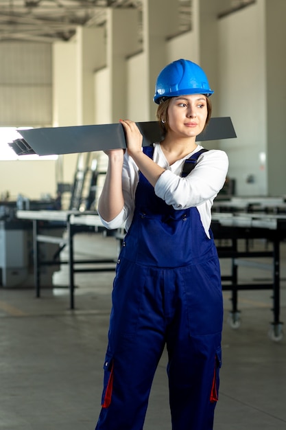 Бесплатное фото Фронтальный вид сбоку молодая привлекательная дама в синем строительном костюме и шлеме, держащая тяжелые металлические детали в дневное время.