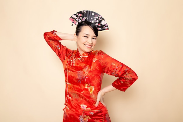 無料写真 伝統的な赤い和服で美しい日本の芸者のヘアスティッククリーム色の背景の日本でエレガントな扇子を保持しているポーズで正面