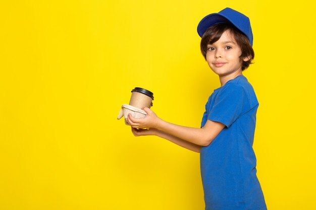 Вид спереди маленького милого курьера в синей футболке, синей кепке с кофейными чашками