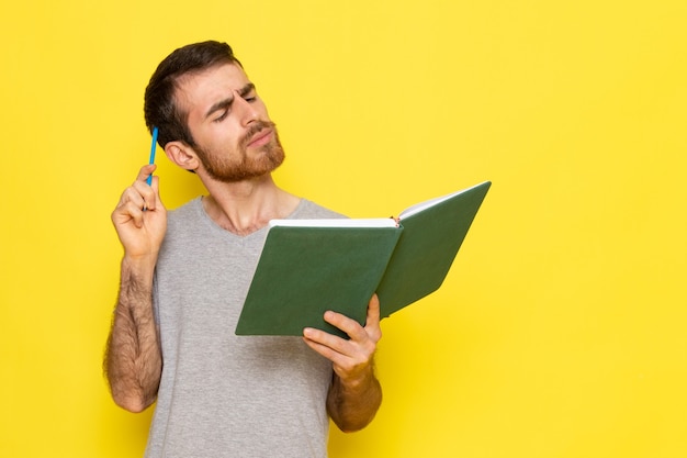 Бесплатное фото Вид спереди молодой мужчина в серой футболке, читающий книгу с выражением мышления на желтой стене, выражение эмоции, цветовая модель человека