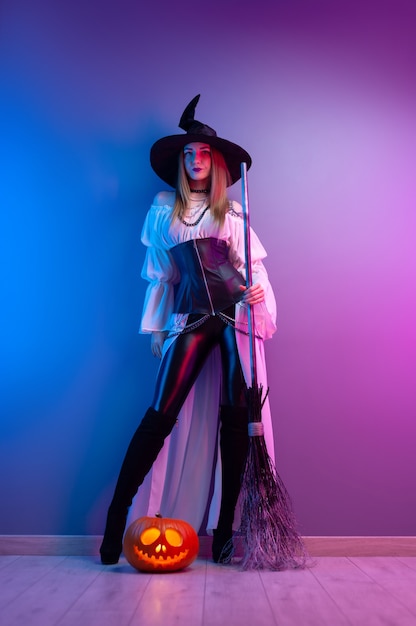할로윈을 위한 마녀 의상을 입은 소녀, 빗자루와 네온 불빛에 호박 프리미엄 사진