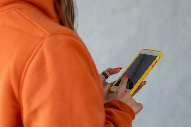 주황색 스웨터를 입은 소녀가 손에 스마트폰을 들고 있다 프리미엄 사진