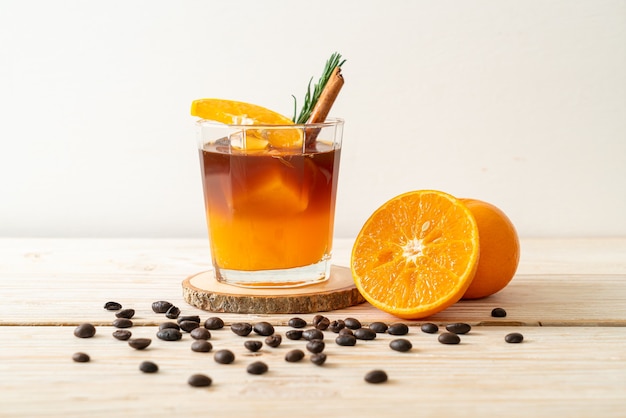 아이스 아메리카노 블랙 커피 한잔과 나무 테이블에 로즈마리와 계피로 장식 된 오렌지와 레몬 주스의 층